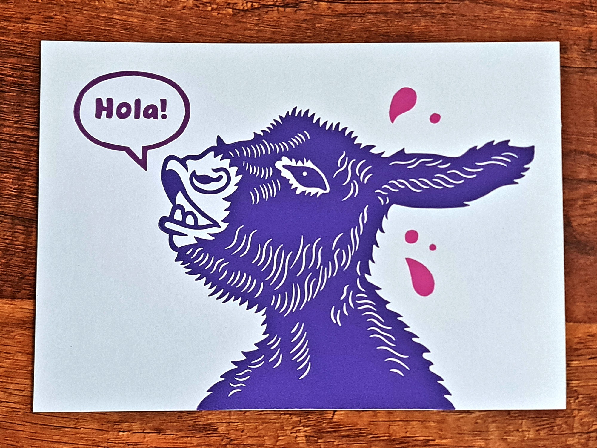 Handgemachter Linoldruck als Wandbild mit einem lila Esel und einer Sprechblase mit dem Text „Hola!“ mit pinken Tropfen auf weißem Hintergund