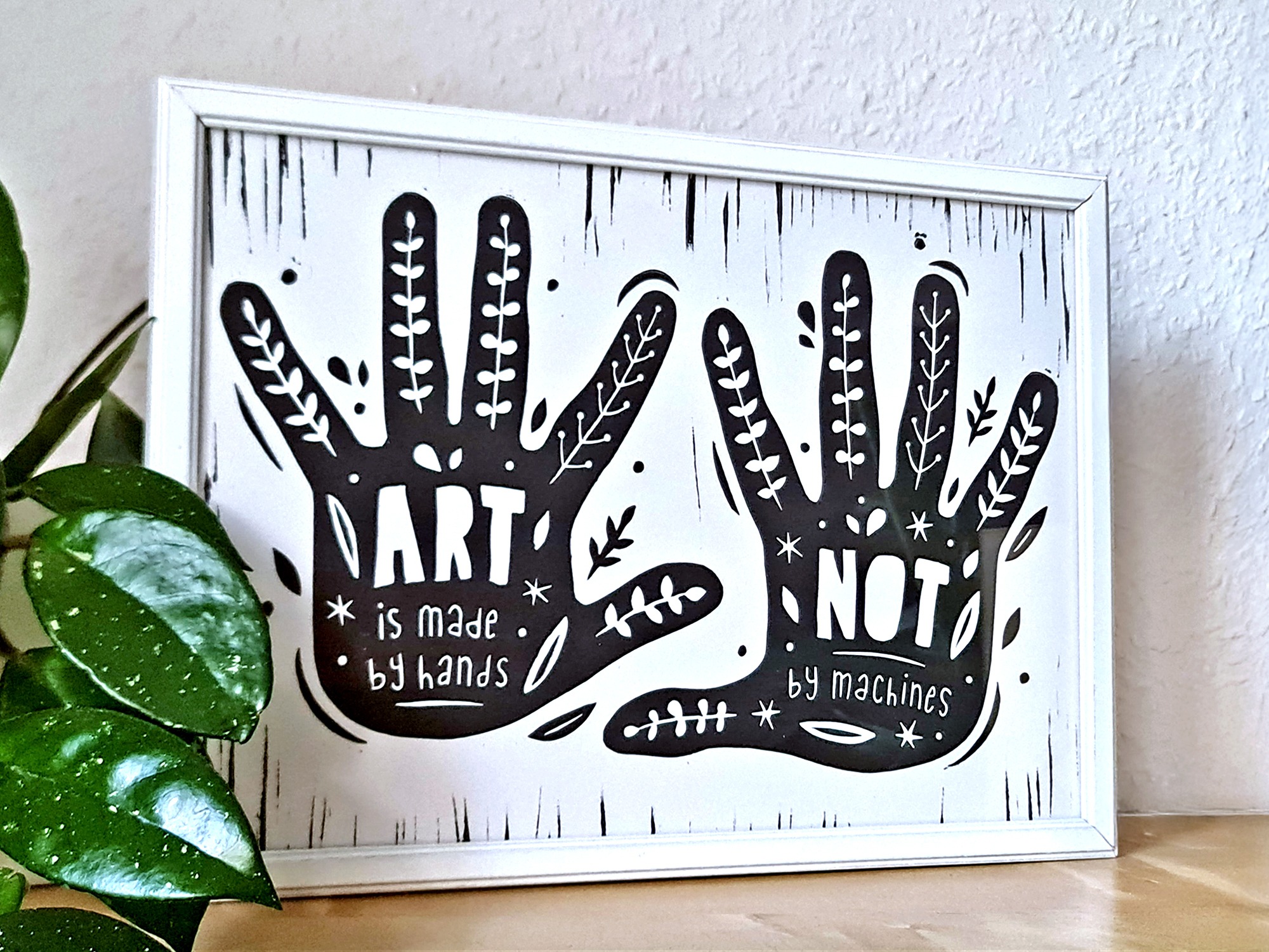 Handgemachter Linoldruck als Wandbild mit zwei Händen, auf denen der Text steht: "Art is mady by hands, not by machines" und Pflanzenranken.