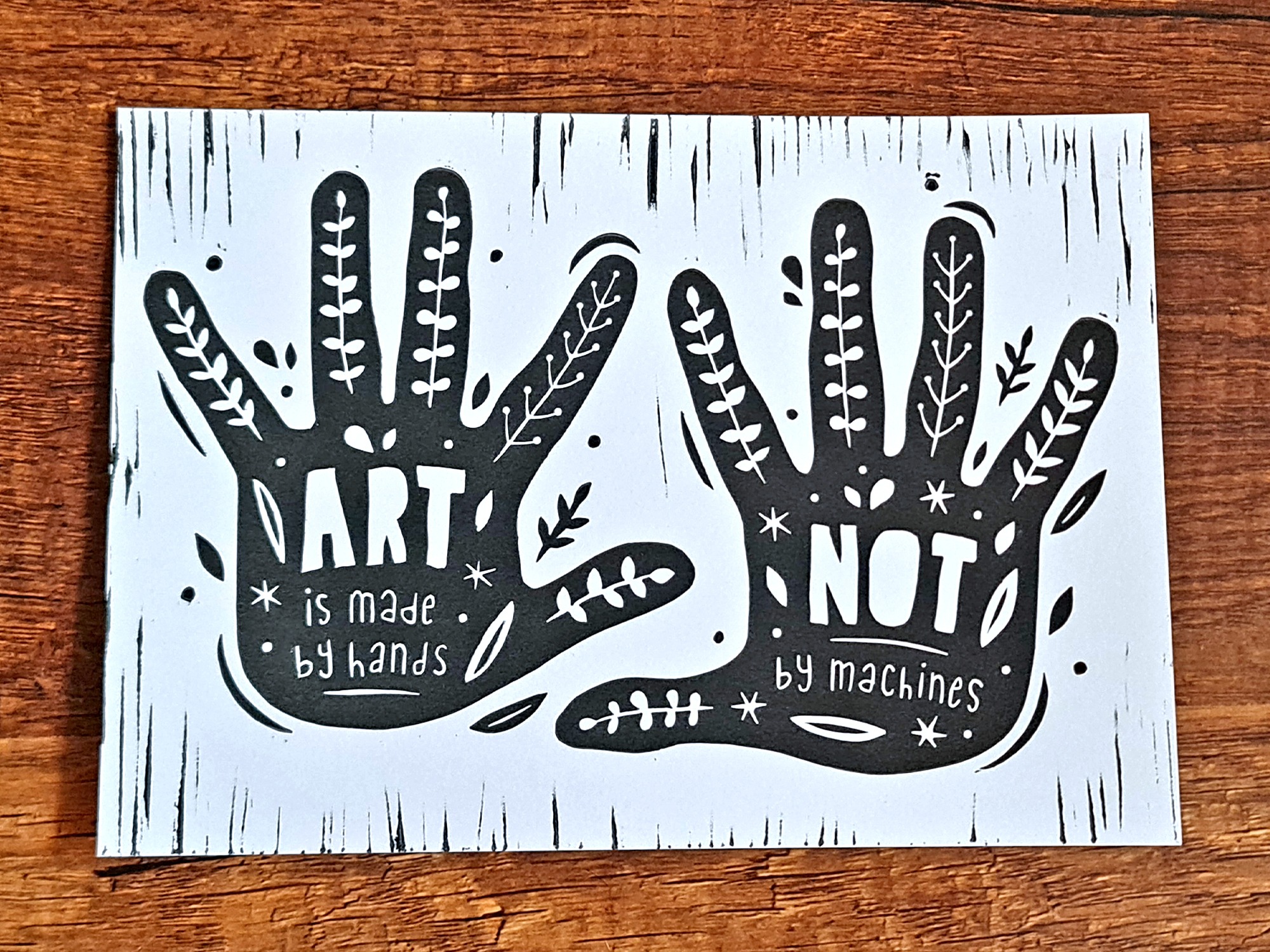 Handgemachter Linoldruck als Wandbild mit zwei Händen, auf denen der Text steht: "Art is mady by hands, not by machines" und Pflanzenranken.