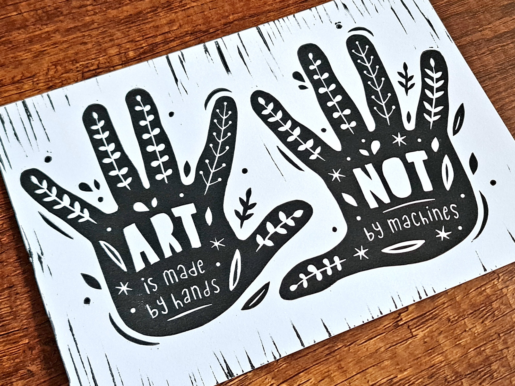 Handgemachter Linoldruck als Wandbild mit zwei Händen, auf denen der Text steht: "Art is mady by hands, not by machines" und Pflanzenranken.