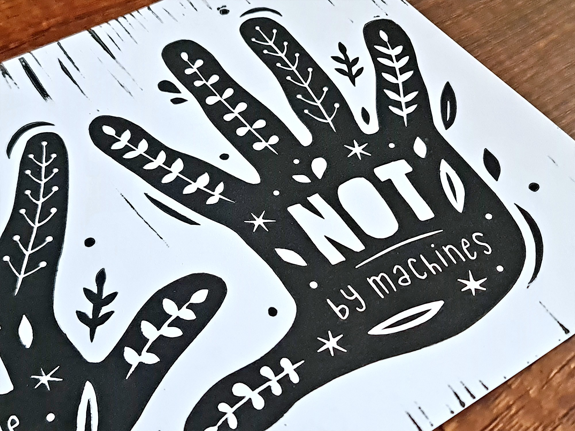 Handgemachter Linoldruck als Wandbild mit zwei Händen, auf denen der Text steht: "Art is mady by hands, not by machines" und Pflanzenranken.