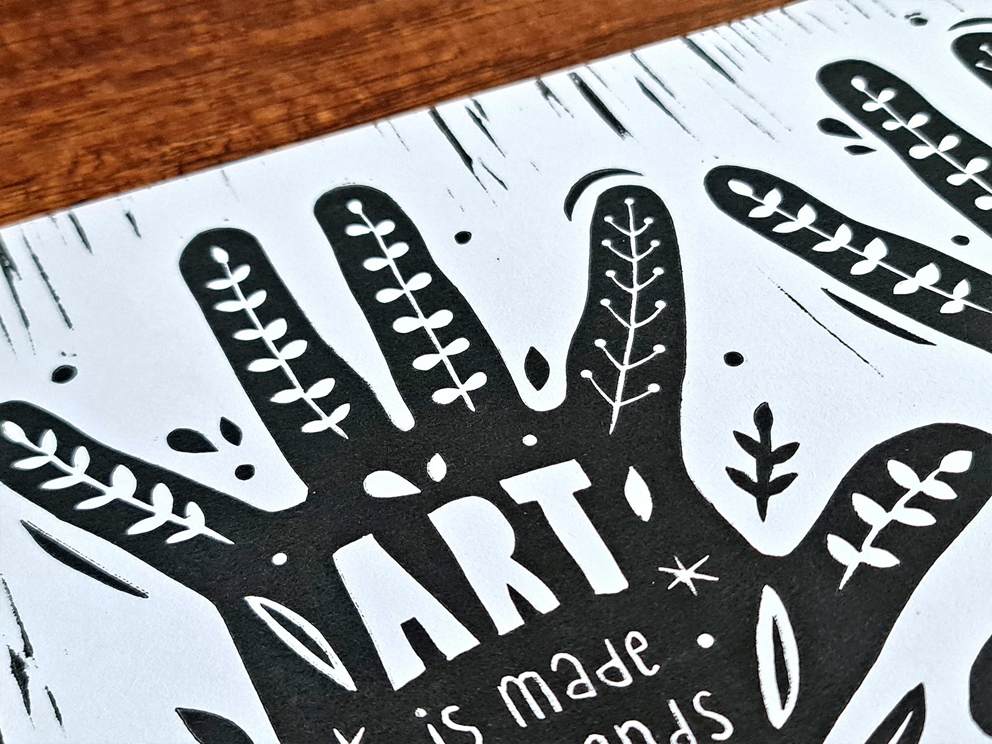 Handgemachter Linoldruck als Wandbild mit zwei Händen, auf denen der Text steht: "Art is mady by hands, not by machines" und Pflanzenranken.